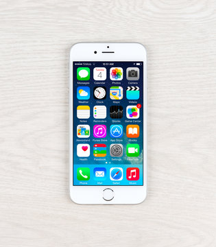 Apple iPhone 6 over table displaying iOS homescreen.