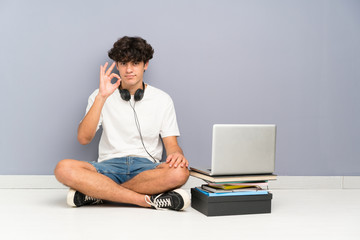 Young man with his laptop sitting one the floor showing an ok sign with fingers