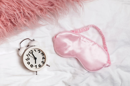 Alarm Clock And Pink Slipping Mask On The Bed,