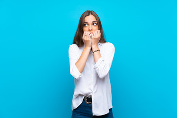Young woman over isolated blue background nervous and scared putting hands to mouth