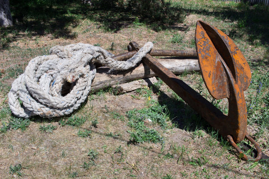 Old rusty iron nautical ship ancor with thick rope laying on ground