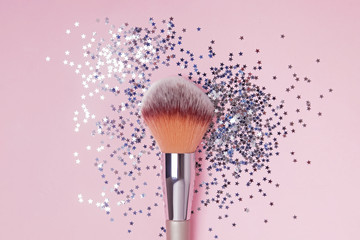 Make-up brush and star shaped confetti on pink backround, top view.