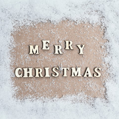 View from above. snow texture. craft paper in the middle with with the inscription merry christmas from wooden letters. Concept