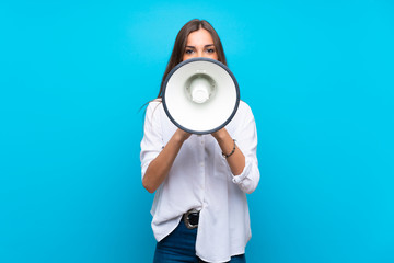 Young woman over isolated blue background shouting through a megaphone
