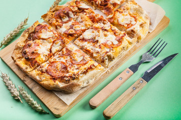Peperroni pizza on a cutting board on a green background. Close-up