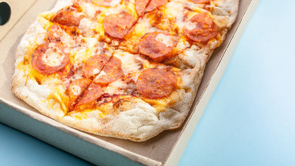 Peperroni pizza in a cardboard box on a blue background. Food delivery concept. Closeup.