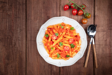 Penne pasta with tomato sauce and parsley, shot from the top on a dark rustic wooden background with copy space
