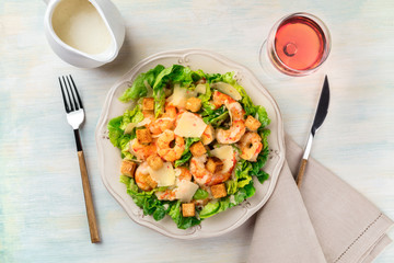 Shrimp Caesar salad with Parmesan cheese, croutons and lettuce, with a glass of rose wine and a gravy boat