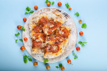 Peperroni pizza on a round cutting board on a blue background. Close-up. Top view