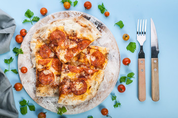 Peperroni pizza on a cutting board on a blue background. Close-up. Top view