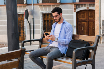 Young businessman is sitting on a bench while he is talking on the mobile