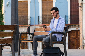 Young businessman is sitting on a bench while he is talking on the mobile