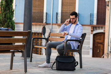 Young businessman is sitting on a bench while he is talking on the mobile