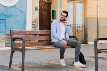 Young businessman is sitting on a bench while he is talking on the mobile