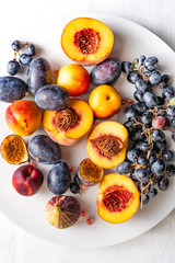 Halved peaches, nectarines, grapes, figs on white plate on white tablecloth, closeup view, top down
