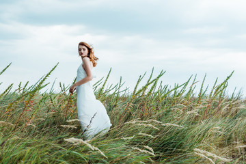 selective focus of attractive redhead woman in white dress looking at camera