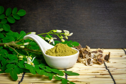Moringa oleifera powder in white ceramic and green leaves on wooden background. Moringa products concept. 