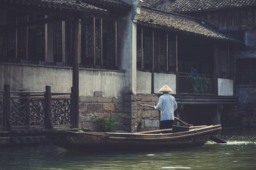 An unidentified Chinese villager travelling in his boat at Wuzheng water town, historic scenic town, in Zhejiang Province, China. Vintage filter. © enchanted_fairy