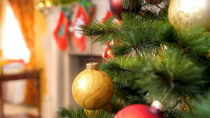 Closeup image of Christmas tree branch decorated with garlands and golden baubles against firepalce with socks for Santa gifts