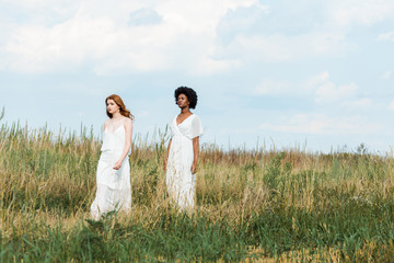 pretty multicultural girls in dresses walking in field
