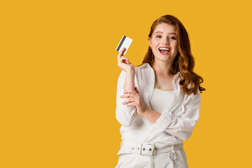 Naklejka premium excited young woman holding credit card isolated on orange