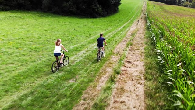 un gar&ccedil;on et une fille de dos font du v&eacute;lo sur un chemin qui longe un champ de ma&iuml;s