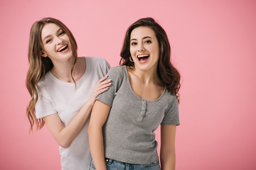 attractive and smiling women in t-shirts looking at camera isolated on pink