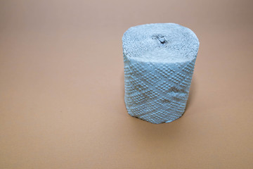 Rough toilet paper role fabricated from recycled paper on brown surface .