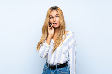 Young blonde woman over isolated blue background keeping a conversation with the mobile phone