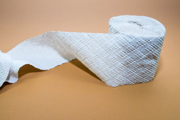 Rough toilet paper role fabricated from recycled paper on brown surface .