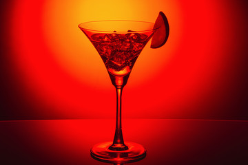 Martini glass with ice on red and yellow abstract background. Selective focus.
