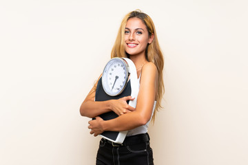 Young blonde woman with weighing machine over isolated background