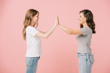 side view of attractive and smiling women in t-shirts giving high five on pink background
