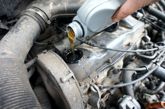 car services. maintenance on vehicle. pouring oil in the car engine