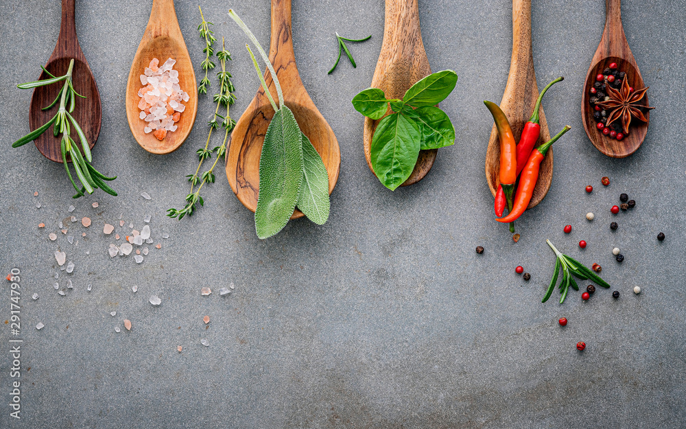 Wall mural Various of spices and herbs in wooden spoons. Flat lay spices ingredients chili ,peppercorn, rosemarry, thyme,star anise ,sage leaves and sweet basil on concrete background.