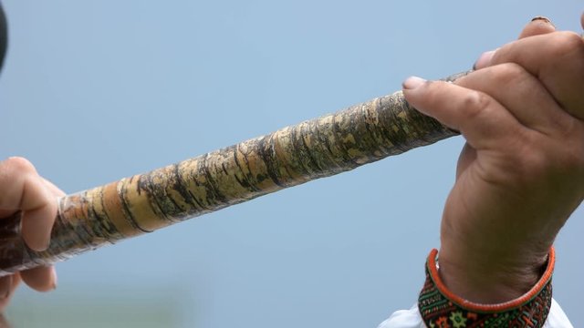 Close up of hutsul man playing trembita. Senior Ukrainian man with musical instrument on blue sky background.