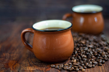 Coffee in brown cups. Hot, invigorating drink. Coffee beans are scattered nearby. In the background homemade cupcakes. 