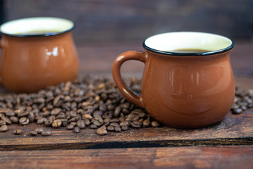 Coffee in brown cups. Hot, invigorating drink. Coffee beans are scattered nearby. In the background homemade cupcakes. 