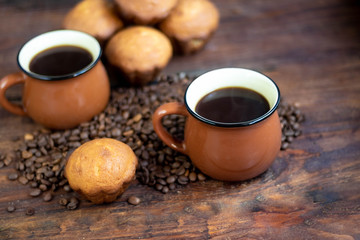 Coffee in brown cups. Hot, invigorating drink. Coffee beans are scattered nearby. In the background homemade cupcakes. 