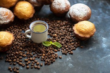 Cup of coffee on a dark background. Brown grains are scattered around the cup, and home-made cupcakes lie. 