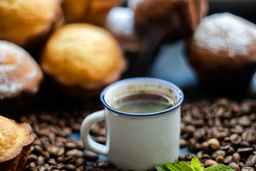 Cup of coffee on a dark background. Brown grains are scattered around the cup, and home-made cupcakes lie. 