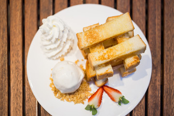 Slices toasts bread with icecream, whipped cream and strawberry on wooden table