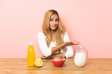 Young blonde woman having breakfast milk extending hands to the side for inviting to come