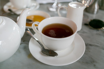 Earl grey tea in white teacup on saucer with teapot, cafe table, close up