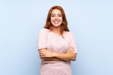 Teenager redhead girl over isolated blue background keeping the arms crossed in frontal position