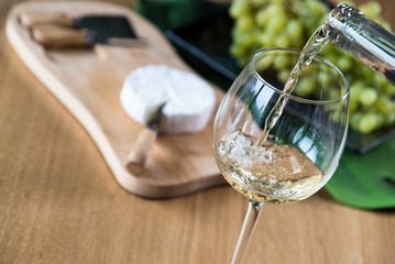 Pouring white wine into the glass against wooden background