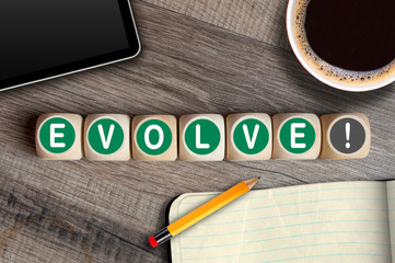 Cubes and dice with word evolve on a workplace desk with cup of coffee, tablet and sketchbook