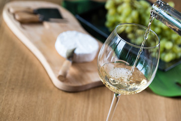 Pouring white wine into the glass against wooden background