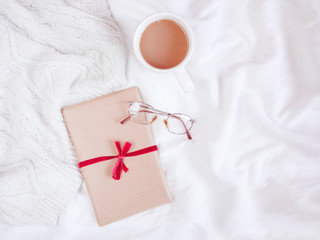 Cup of coffee or tea next to a knitted sweater and a present isolated on white linen background. Flat lay. Top view. Copy space