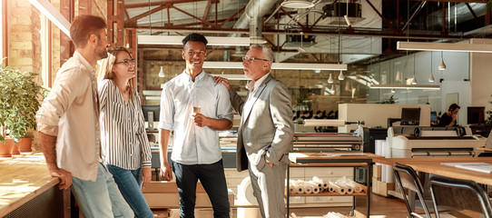 Project done. Business people holding coffee cups and talking about something with smile while standing in the modern office